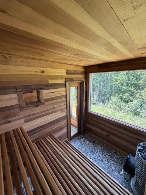Sauna interior with tiered cedar benches, a wood-clad ceiling, and a large window onto the forest